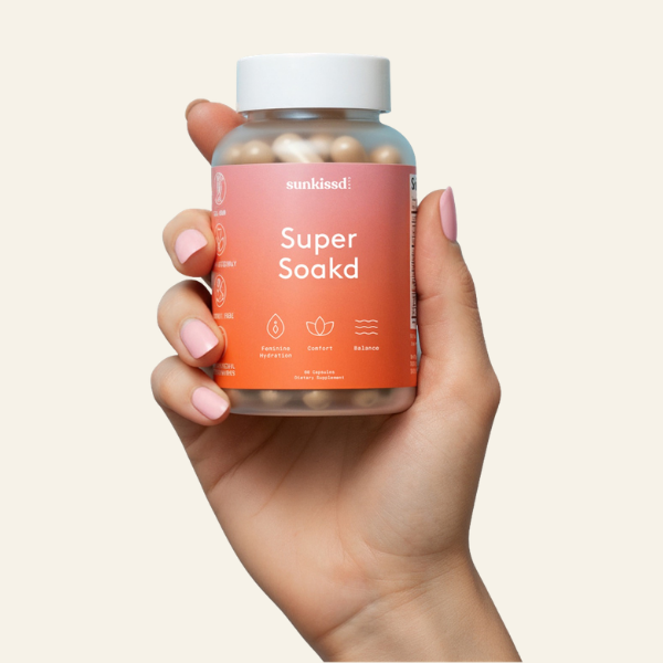 Hand holding a bottle of 'Super Soakd' supplements with a plain background