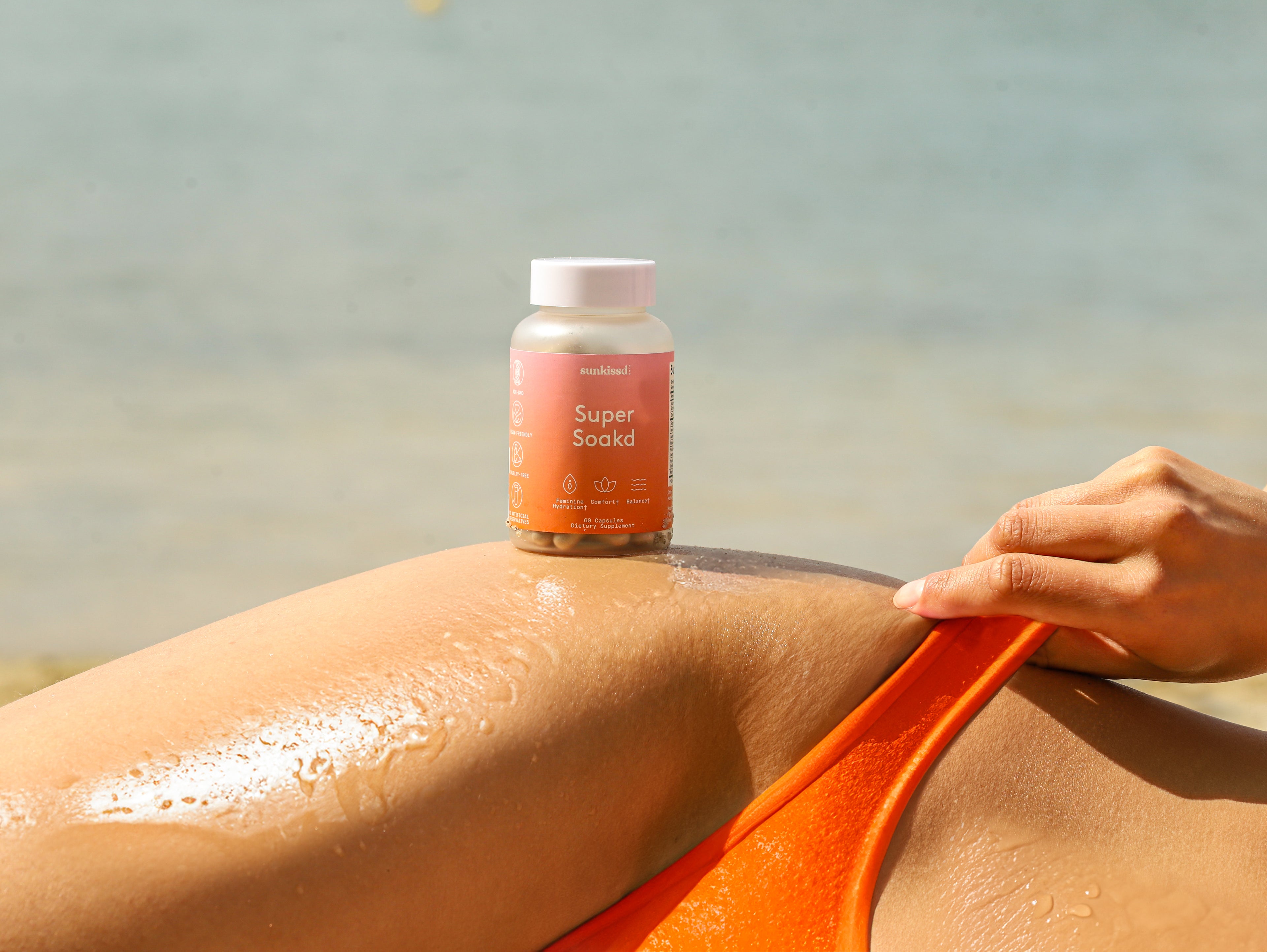 Person applying a bottle labeled 'Super Soaks' to their skin by the beach.