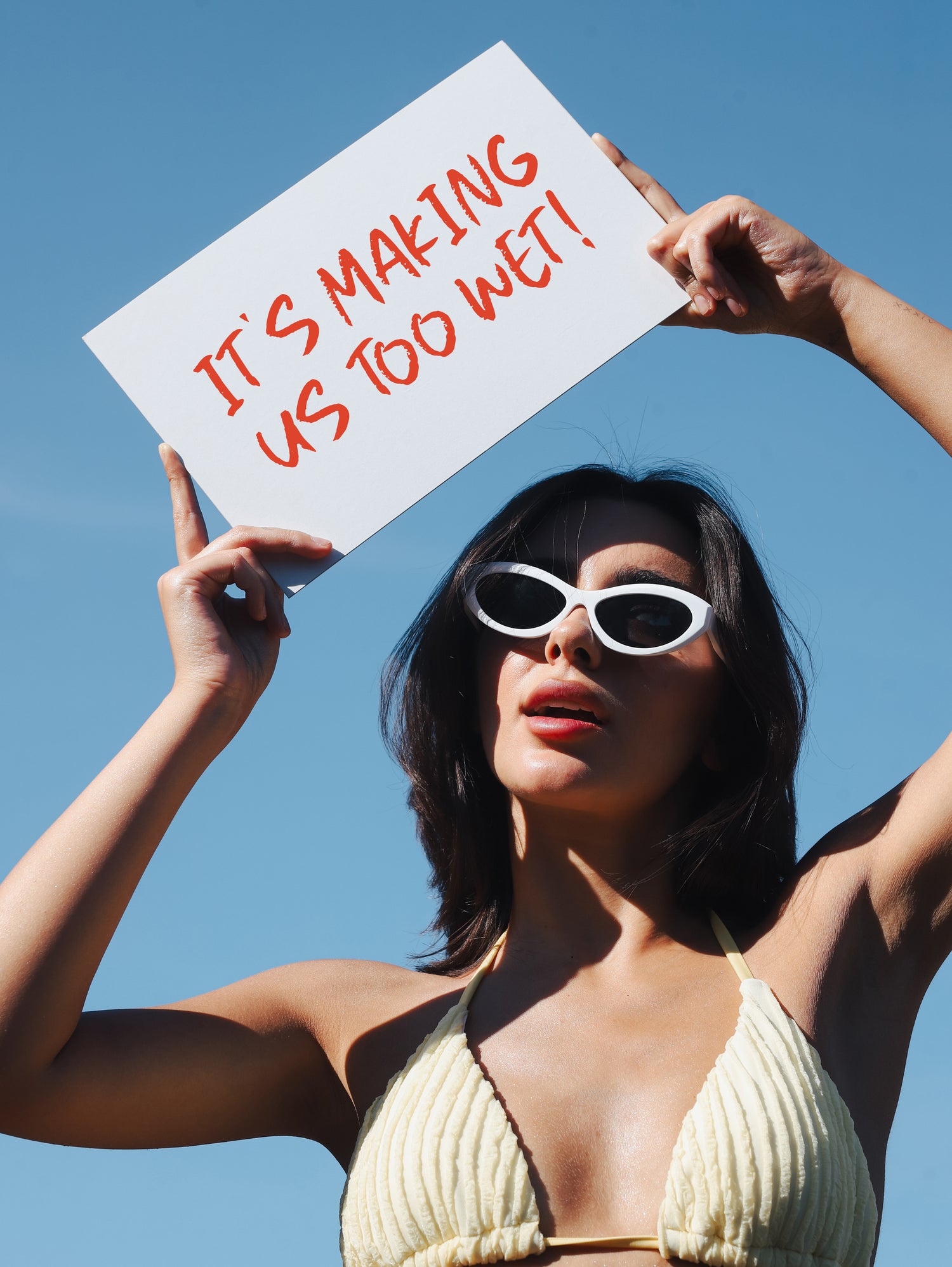 Woman in a bikini holding a sign with text against a clear blue sky