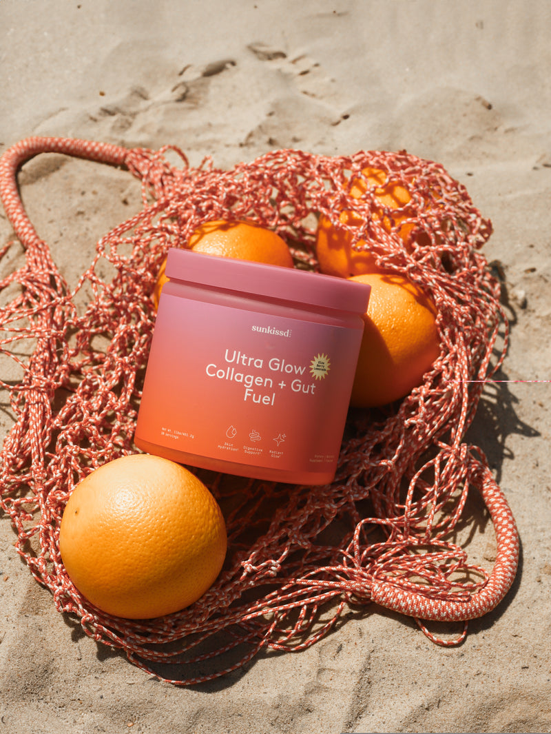 Pink container labeled 'Ultra Glow Collagen + Gut Fuel' surrounded by oranges on a textured surface