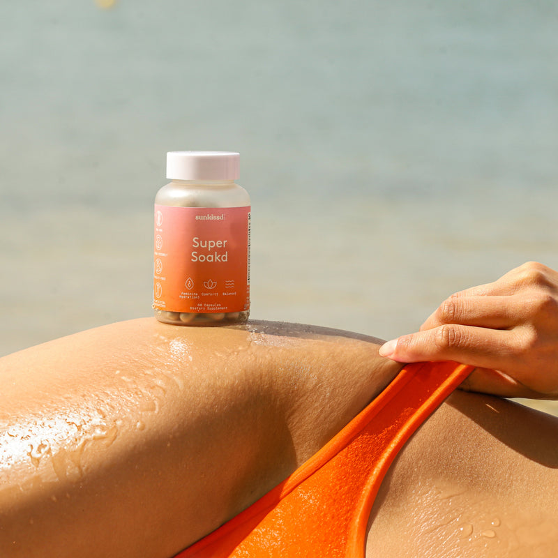 Person applying a bottle labeled 'Super Soaks' to their skin with a beach background
