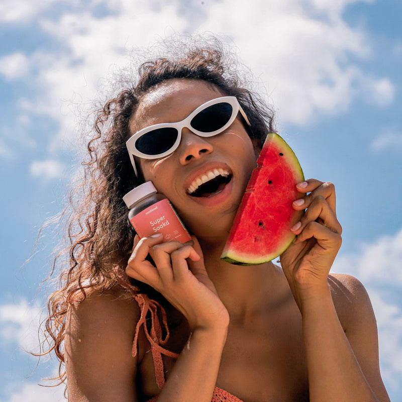 Woman holding a watermelon slice and a coffee cup against a blue sky.