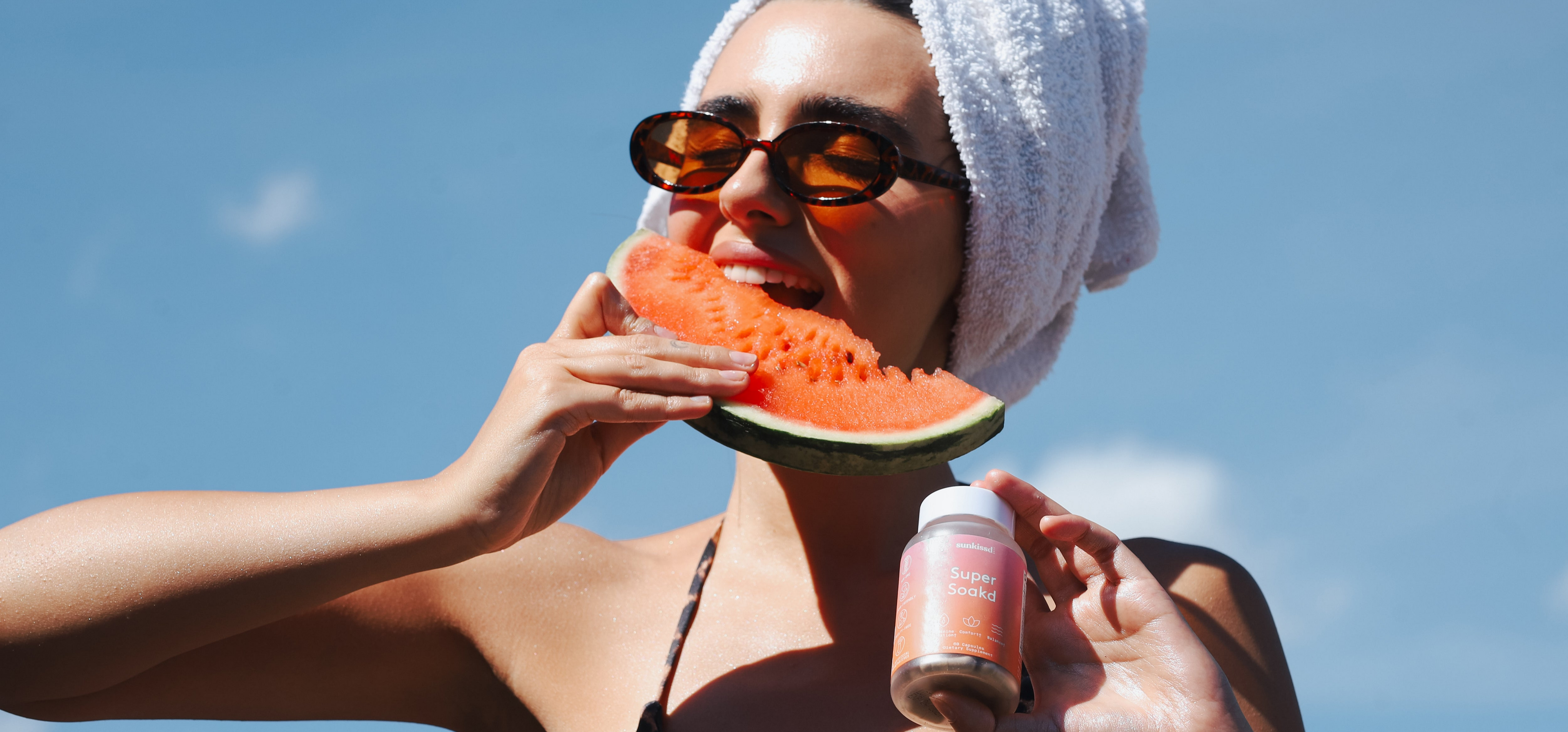 Woman eating watermelon and holding a bottle against a clear blue sky