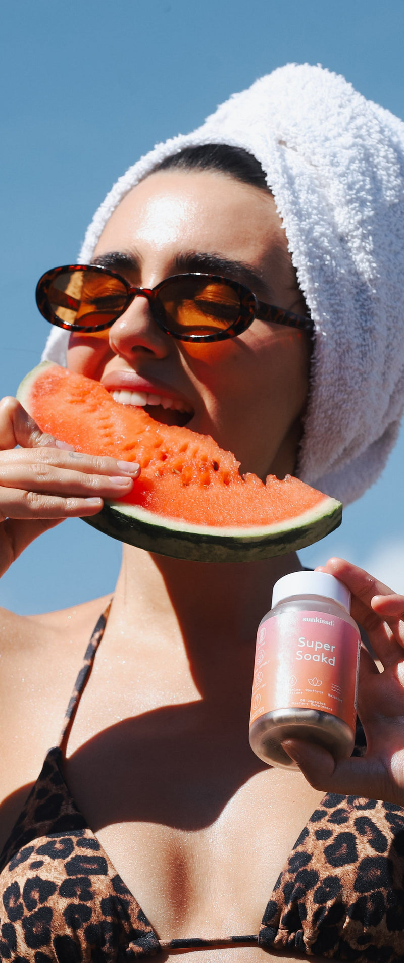 Woman eating watermelon and holding a bottle against a blue sky background