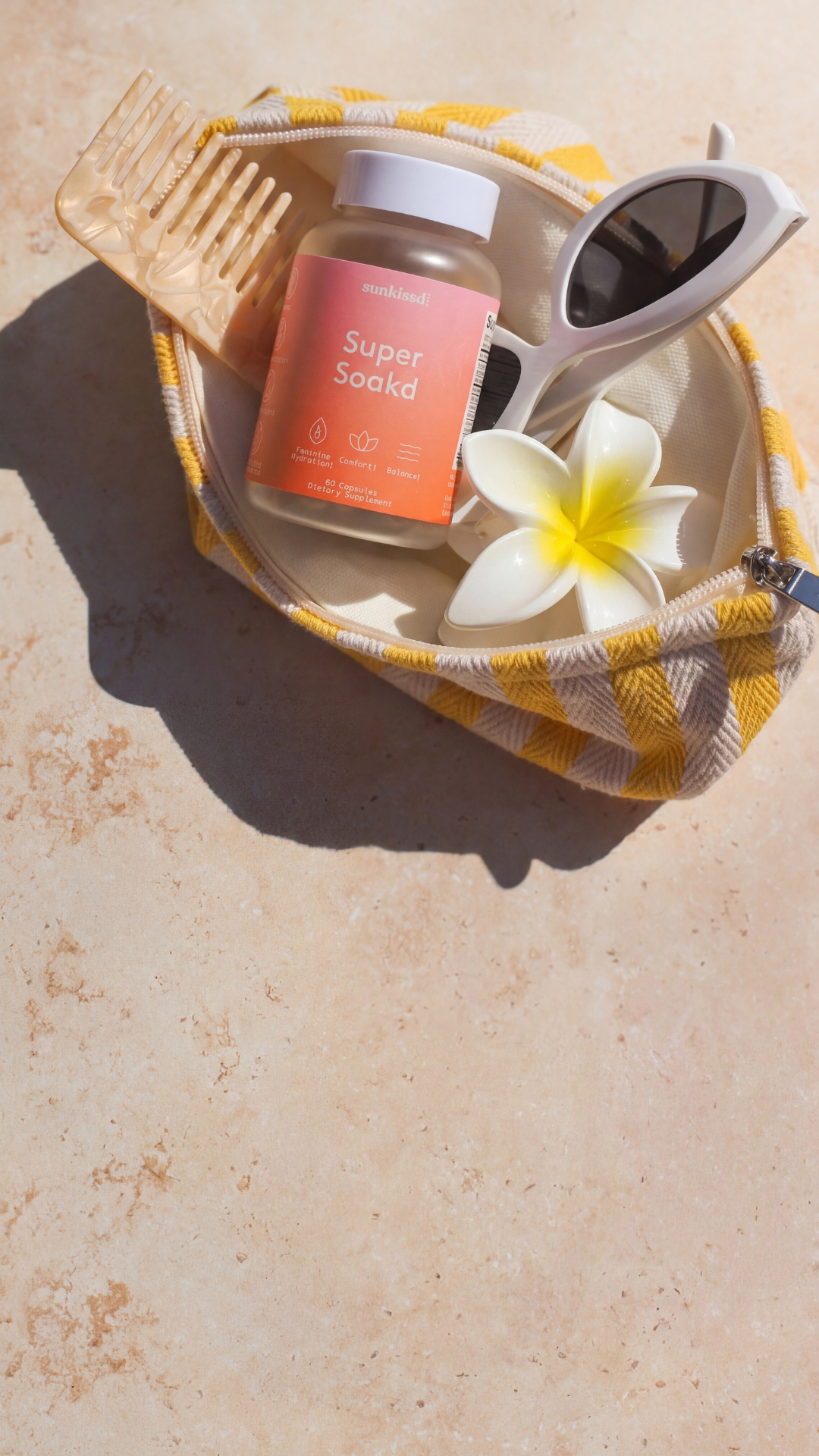 Sunscreen bottle, comb, and sunglasses on a towel with a flower, all on a textured surface.