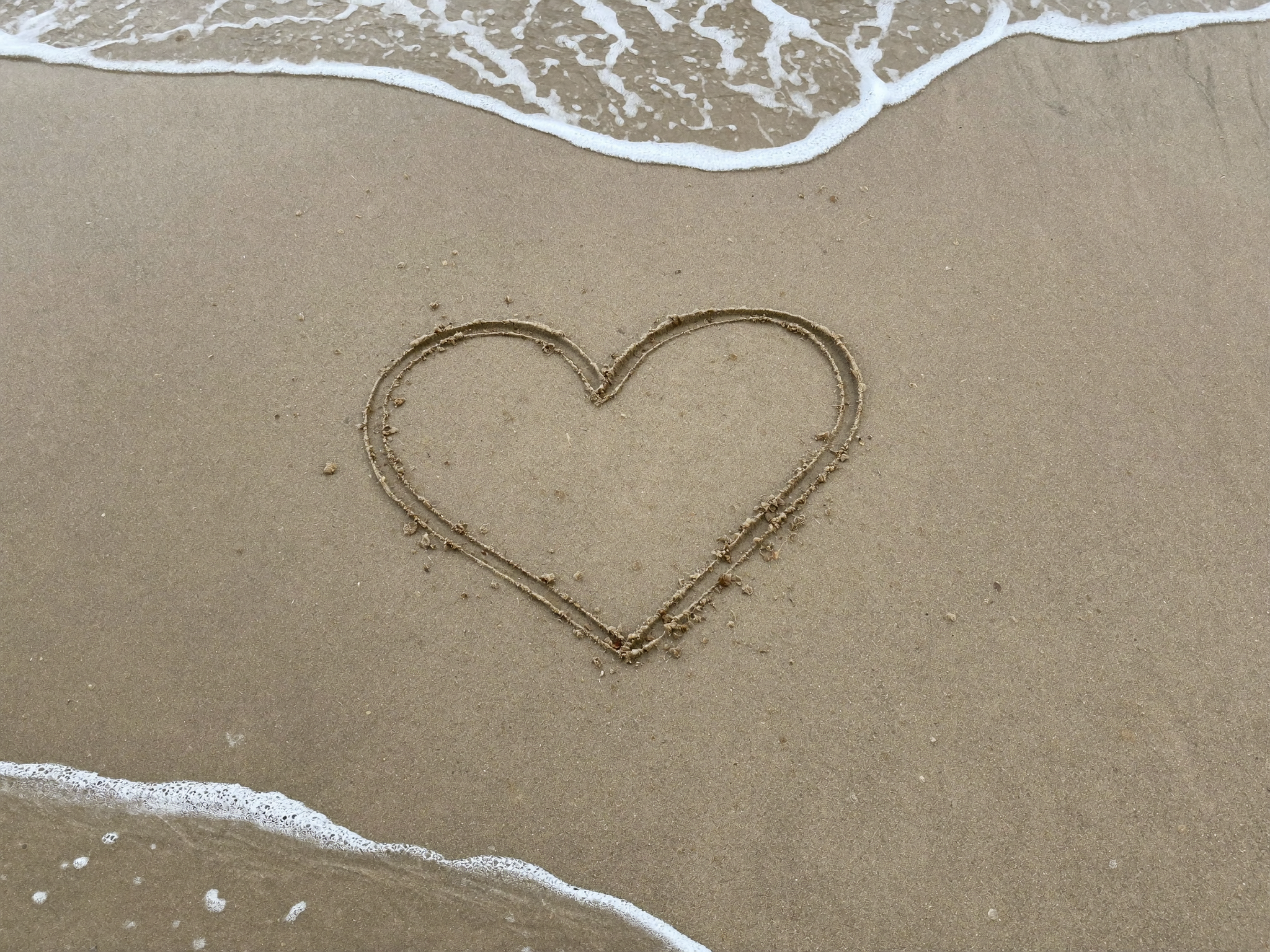 Heart shape drawn in sand on a beach with waves.