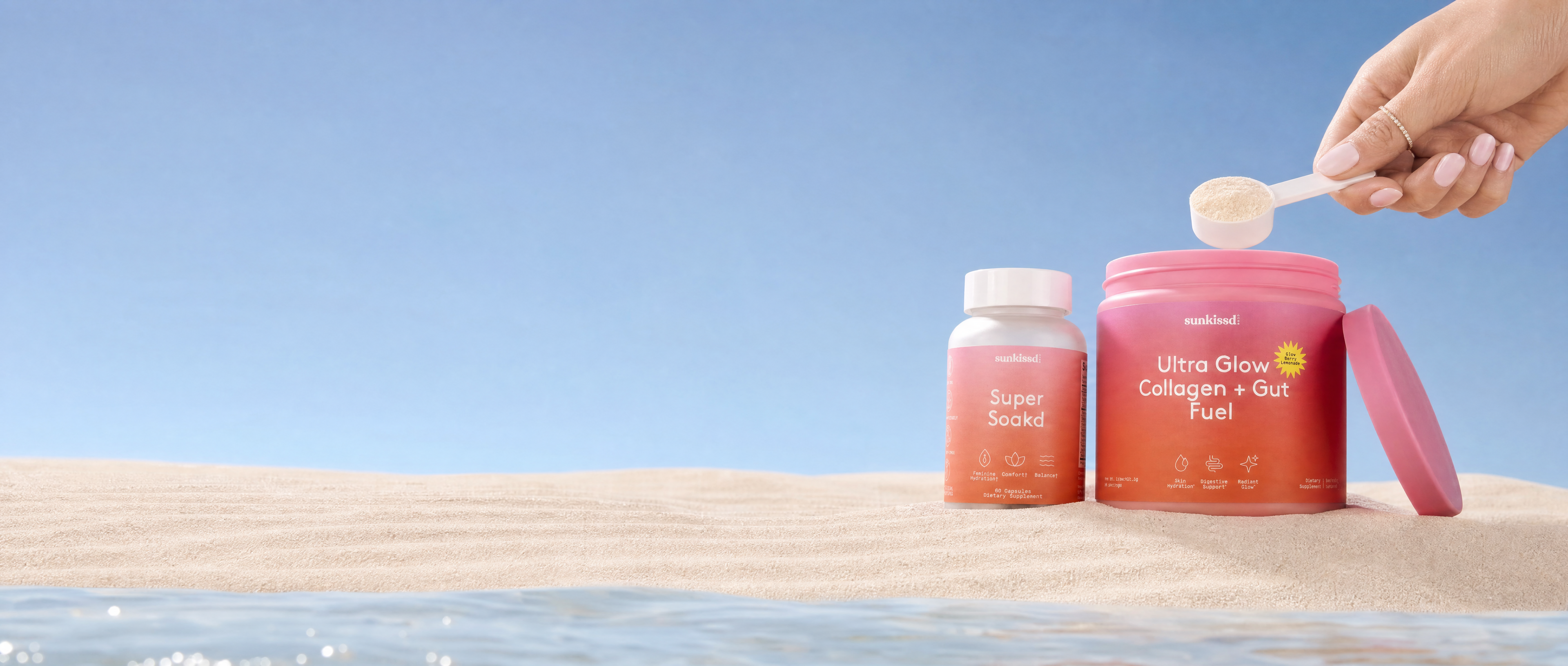 Two pink supplement bottles on a sandy beach with a person's hand holding a spoon above the larger bottle, which reads 'Ultra Glow Collagen + Gut Fuel'.